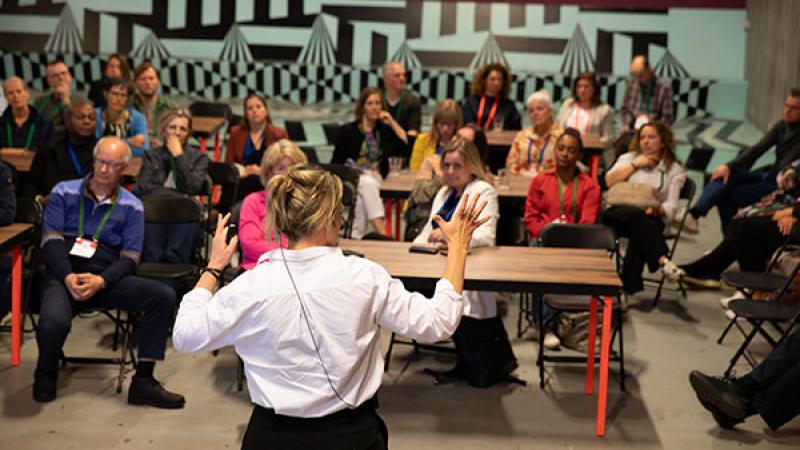 Groep mensen aan tafels luisteren naar een docent