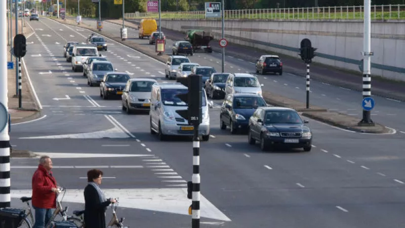 Kruispunt waarop 2 fietsers wachten bij het verkeerslicht terwijl auto's voorbij rijden